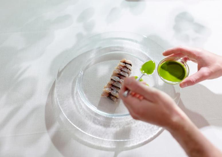 Mani versano salsa verde su piatto raffinato, atmosfera elegante e creativa.